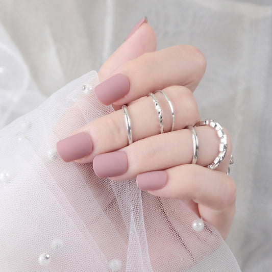 A set of medium oval-shaped, matte mauve press-on nails with a unique textured finish, displayed on a hand holding a sheer fabric.