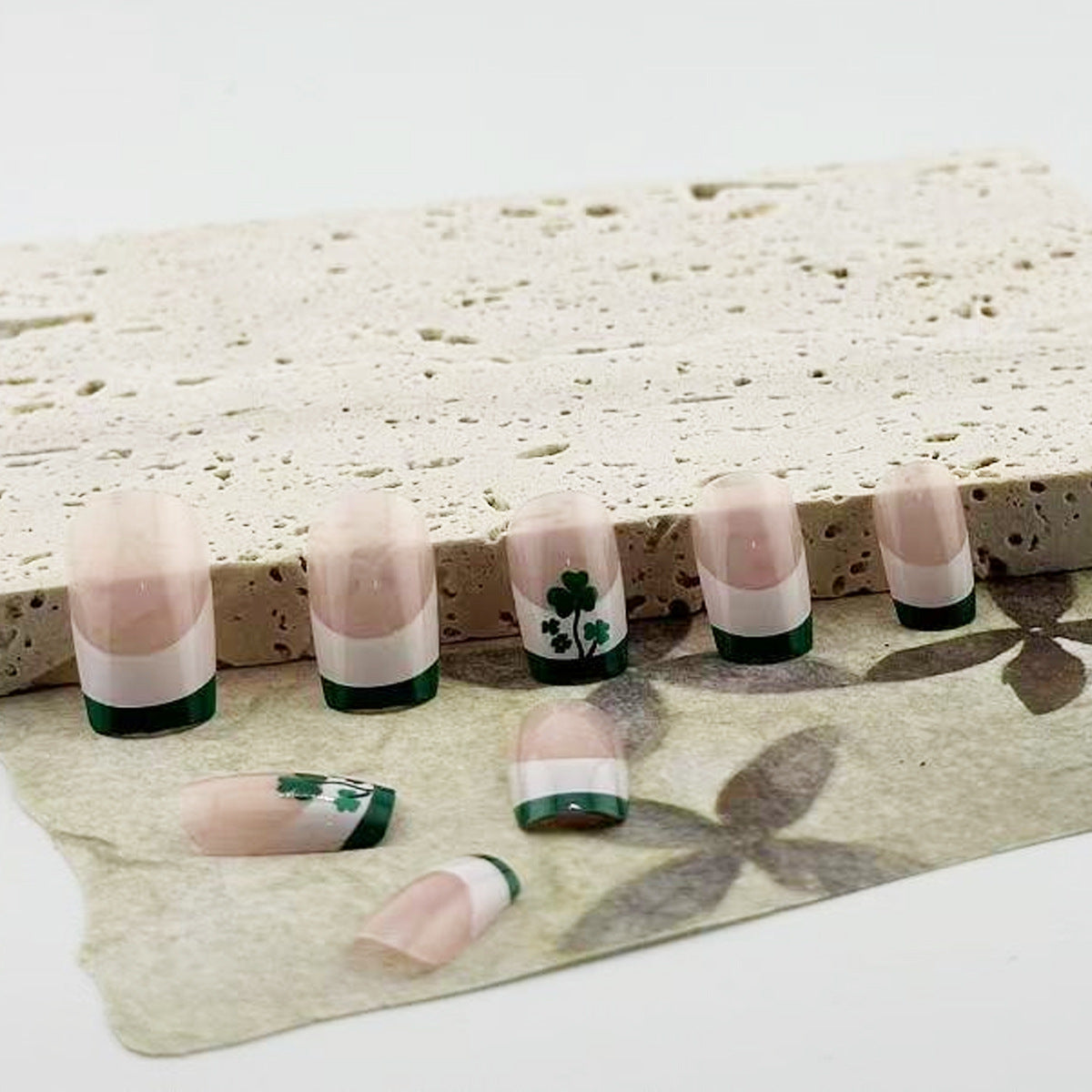 A set of false nails laid out on a surface, featuring a beige and green color scheme with a unique clover design.