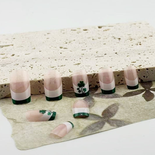 A set of false nails laid out on a surface, featuring a beige and green color scheme with a unique clover design.