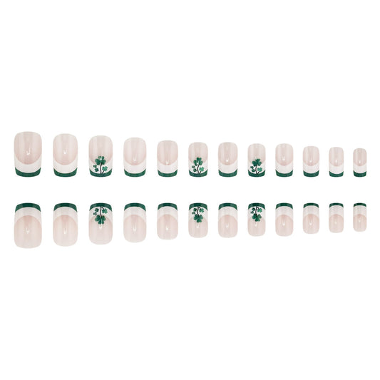 A set of false nails laid out in a row, featuring a clear nail polish base with a green stripe and shamrock design.