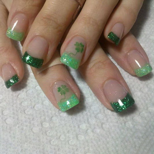 Nails with green glitter and shamrock designs on a textured white background