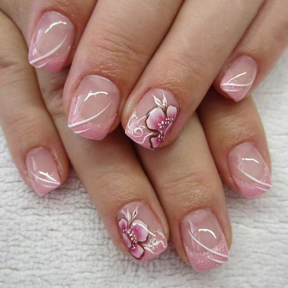 A set of press-on nails featuring a soft pink color with elegant floral designs and a shimmer finish.
