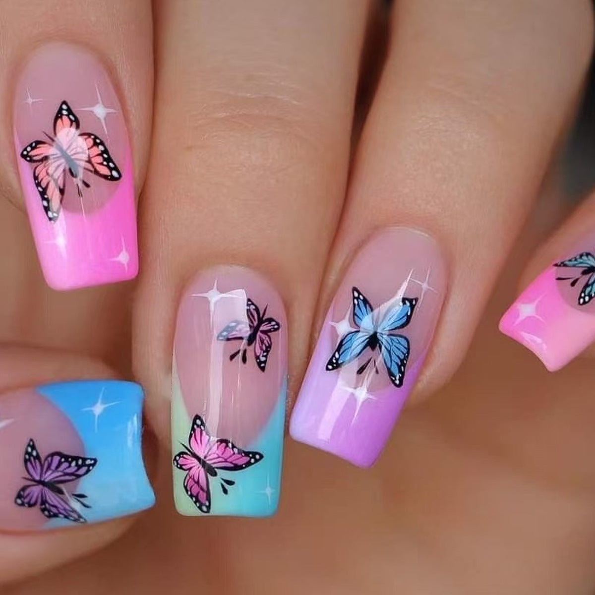 Nails with butterfly designs in pink, blue, and purple on a light background