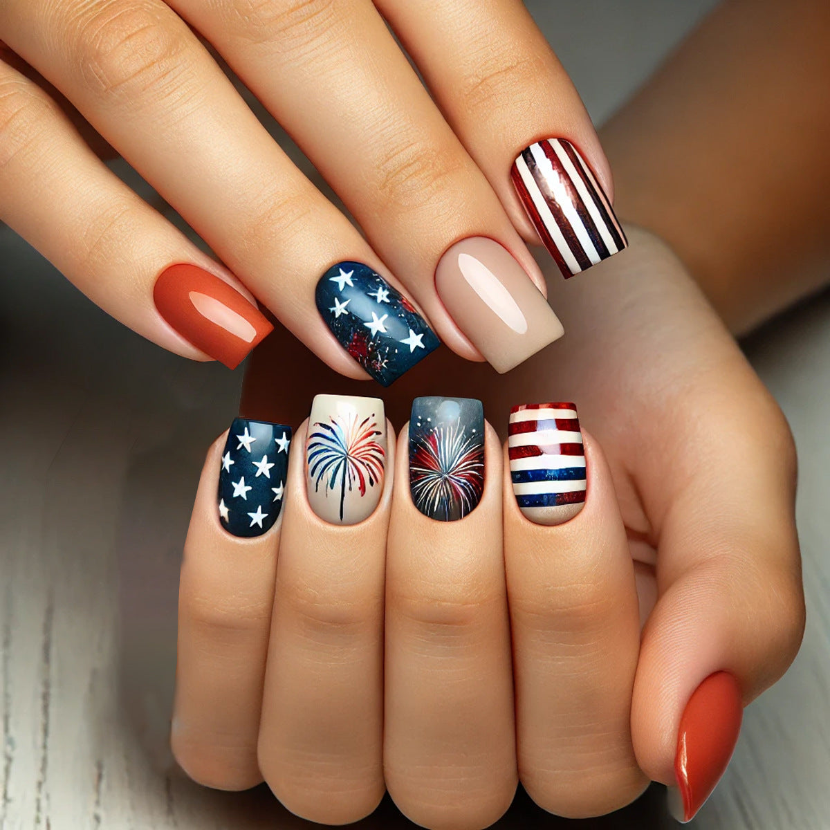 Hand with nails featuring various patriotic nail art designs on a neutral background