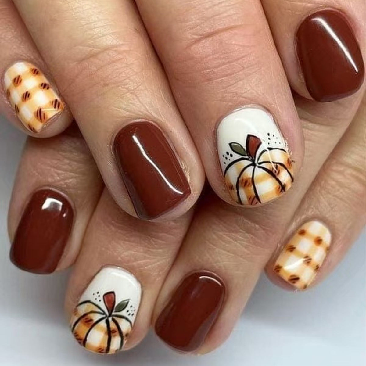 Nails with brown polish and pumpkin designs on a white background