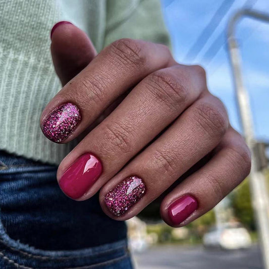 Close-up of a hand with pink glittery nail polish against a blurred outdoor background