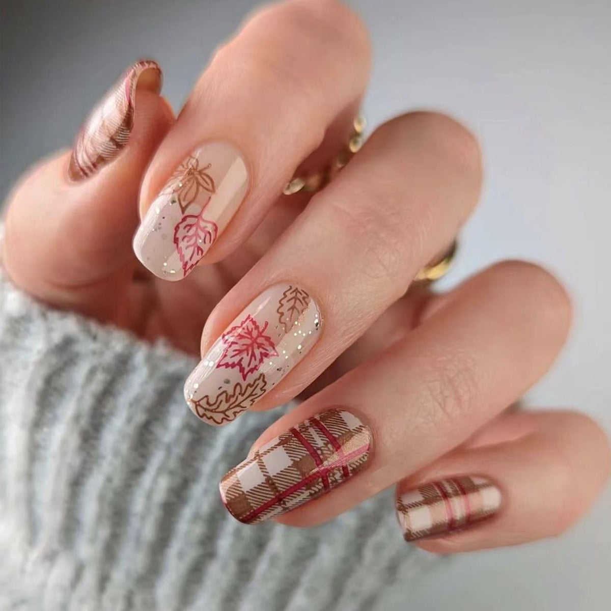 Nails with autumn-themed design featuring leaves and plaid patterns.
