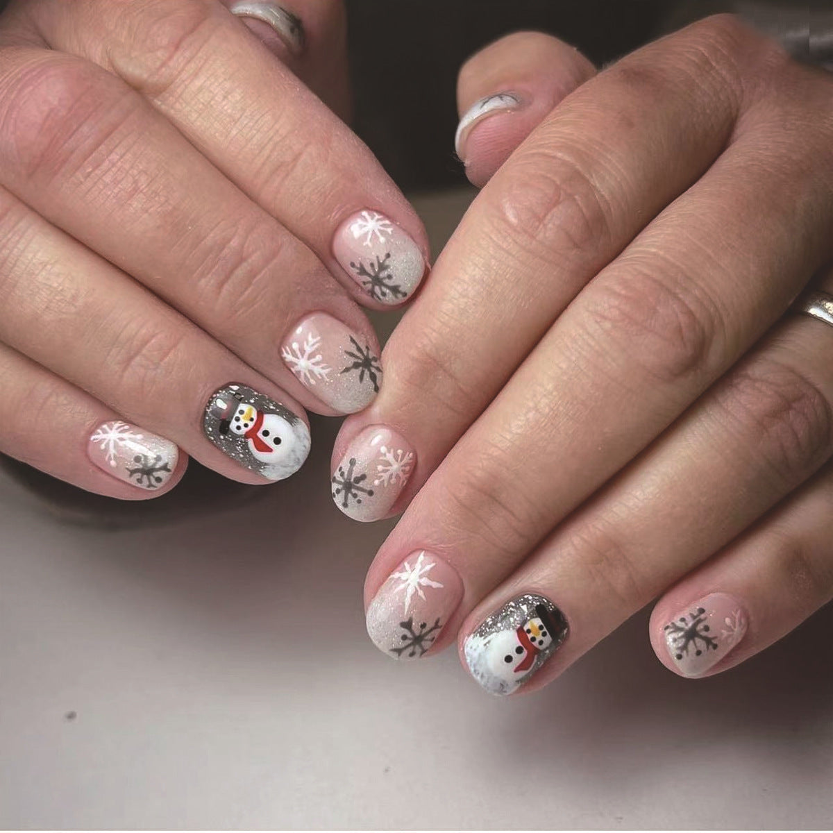 A set of press-on nails featuring a winter theme with designs including a snowman and snowflakes, in white, silver, and other colors.