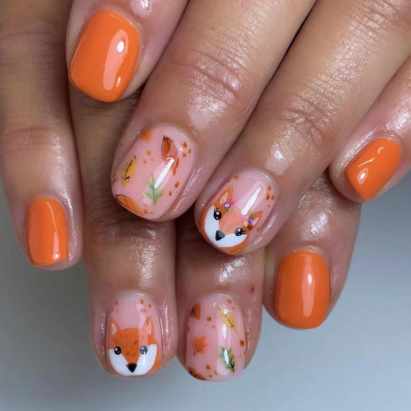Nails with fox design and orange polish on a neutral background