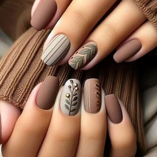 A set of medium square matte nails with brown color and botanical accents, such as leaves and stripes.