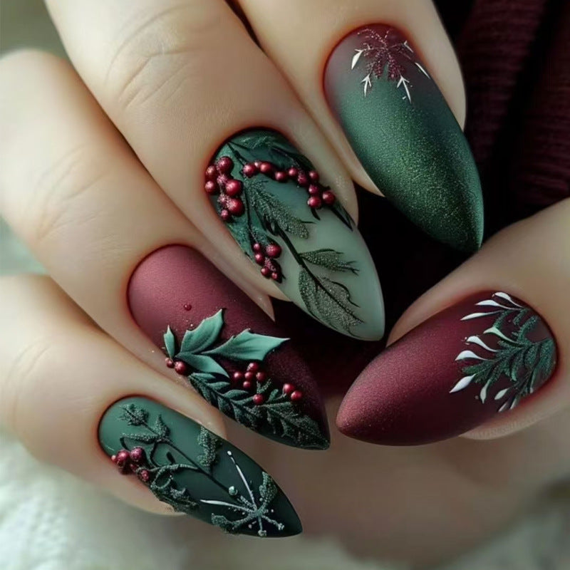 A set of press-on nails featuring an almond shape with a matte green and burgundy color scheme, adorned with intricate holiday leaf designs and red berries.