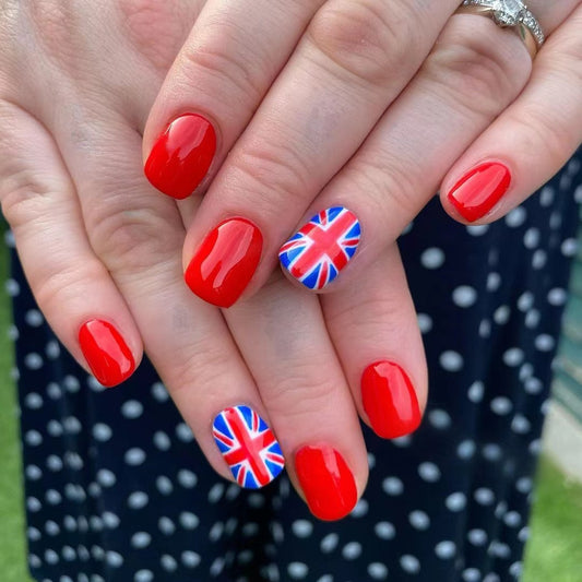 A set of medium oval red press-on nails with union jack accents, shown in a polished state on a person's hands against a dotted background.