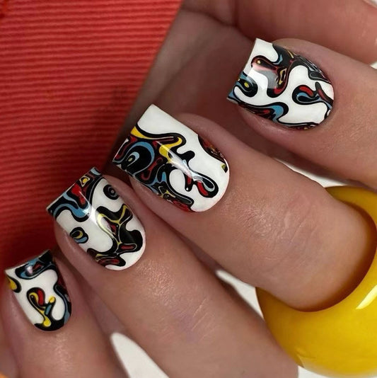 A set of long, multicolored press-on nails with a vibrant square swirl pattern, displayed on a human hand.