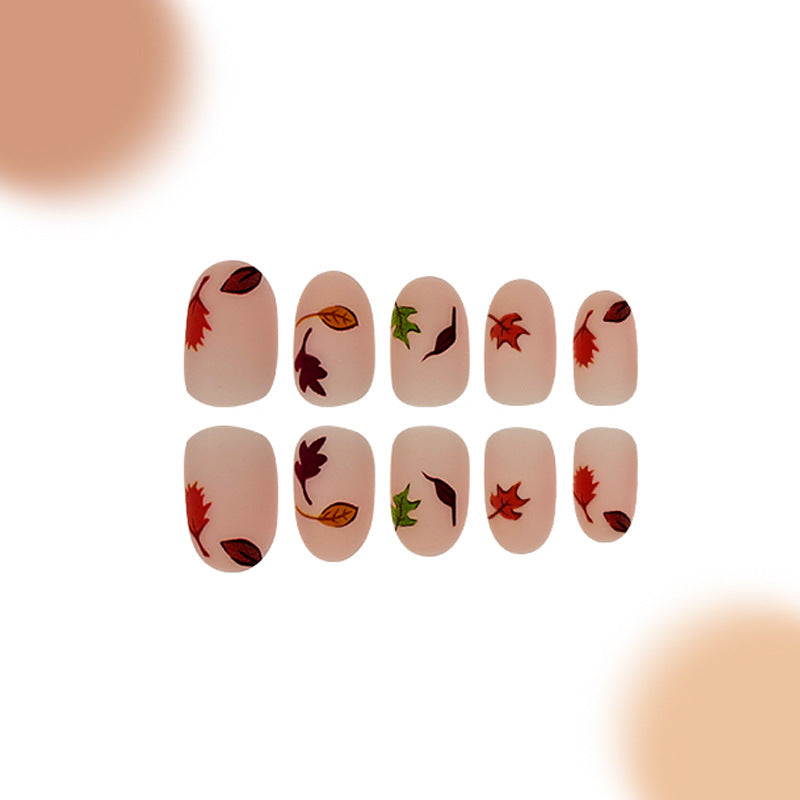 A set of beige press-on nails with leaf patterns, arranged in a line.