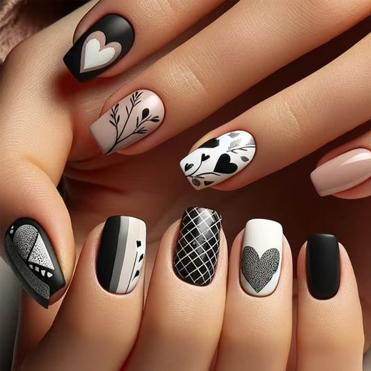 A set of press-on nails featuring black and white floral and heart designs on a square-shaped nail.