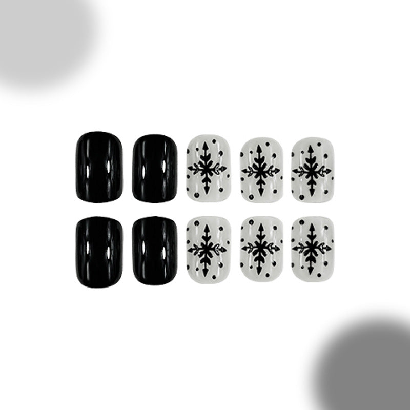 A set of four press-on nails in black and a set of four press-on nails in white, both featuring a snowflake pattern.