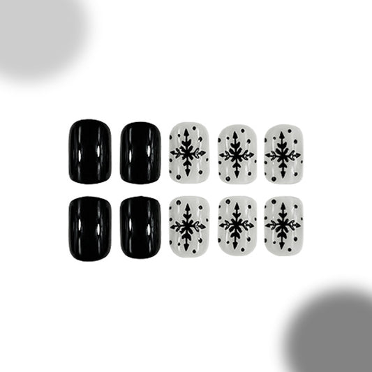 A set of four press-on nails in black and a set of four press-on nails in white, both featuring a snowflake pattern.
