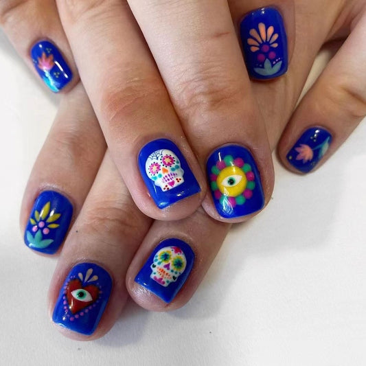 A set of press-on nails featuring a variety of colorful designs, including a sugar skull, flowers, and hearts in a deep blue color.