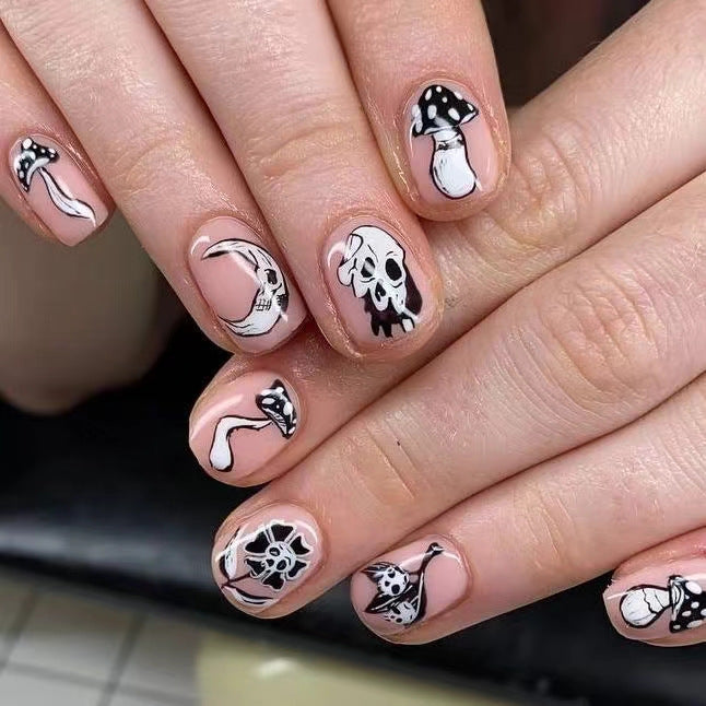 A set of oval-shaped natural pink press-on nails with a skull and mushroom design.