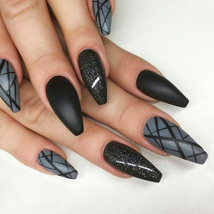 A set of long, black press-on nails with gray patterns and glittering accents, displayed on a hand.