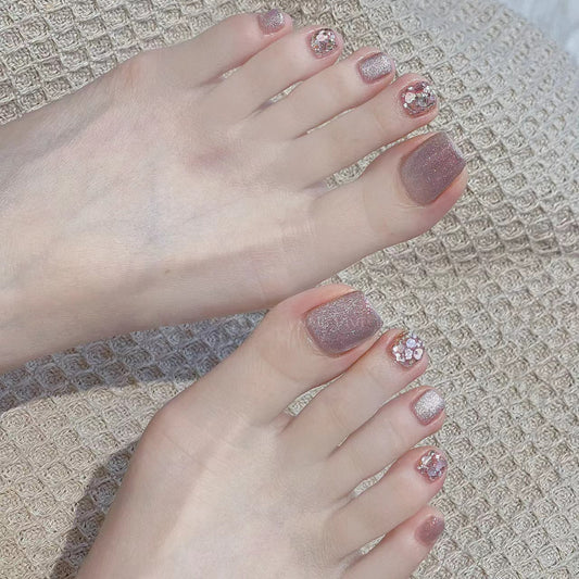 Close-up of feet with glittery pink nail polish on a textured surface