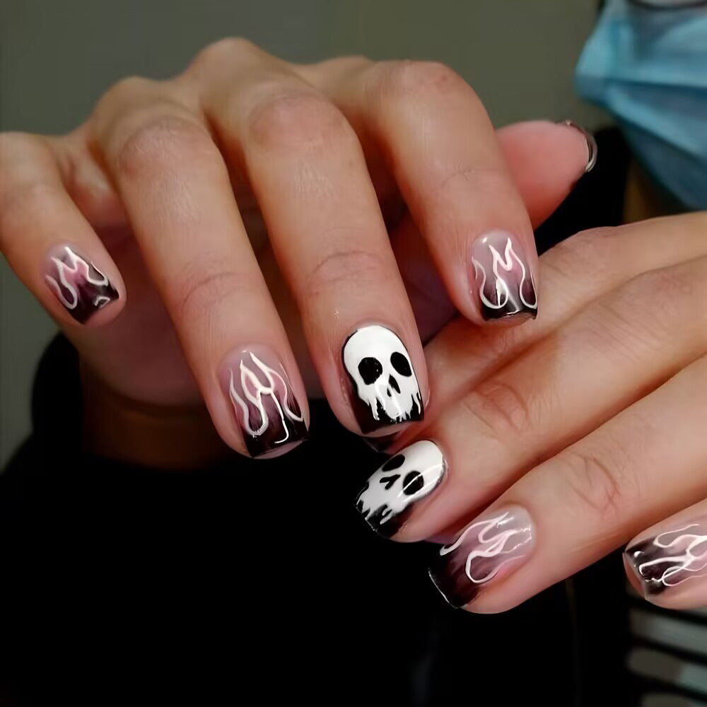 A set of press-on nails featuring a black and pink flame design with a skull accent, displayed on a person's hand.