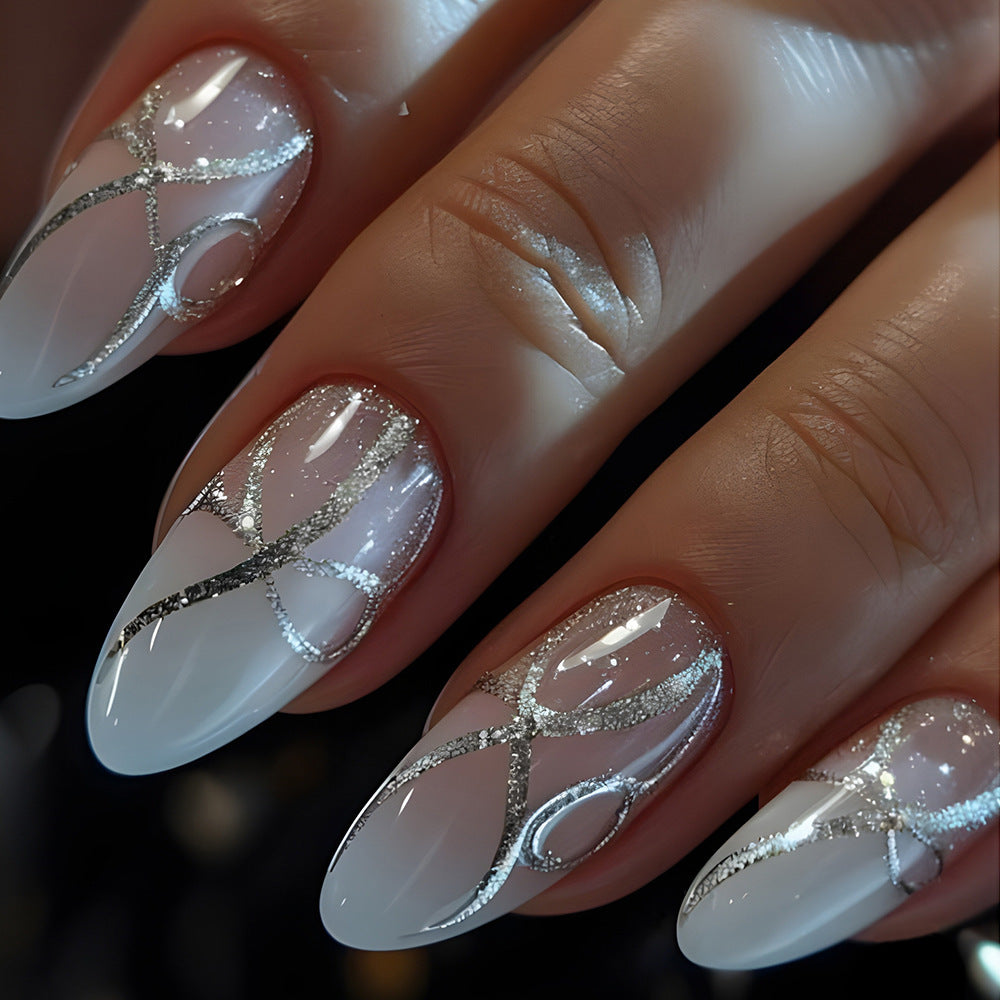 A set of press-on nails with a white base and silver swirl and stripe design, displayed on a hand.