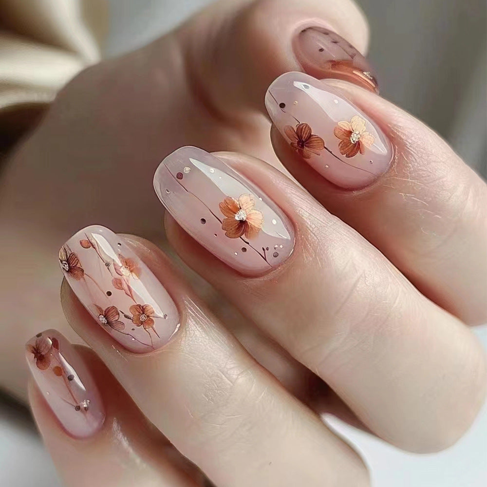 A set of press-on nails featuring a floral design with pink and white flowers and sparkling details.