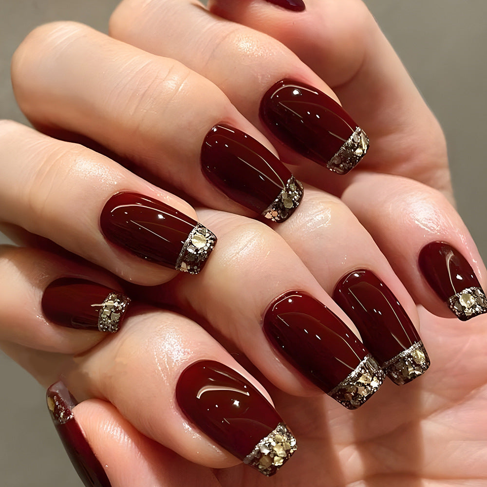 A set of burgundy press-on nails with diamond accents, displayed on a hand.
