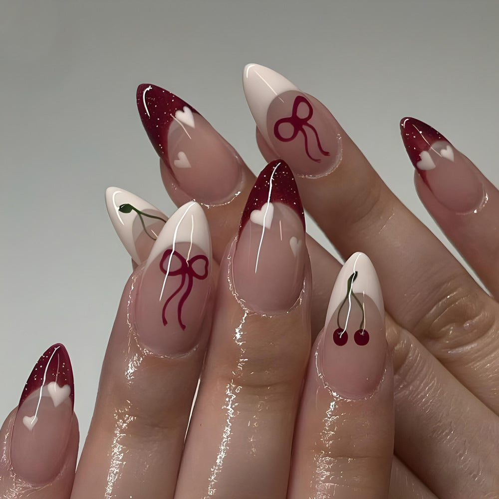 Nails with artistic designs including bows and cherries on a neutral background