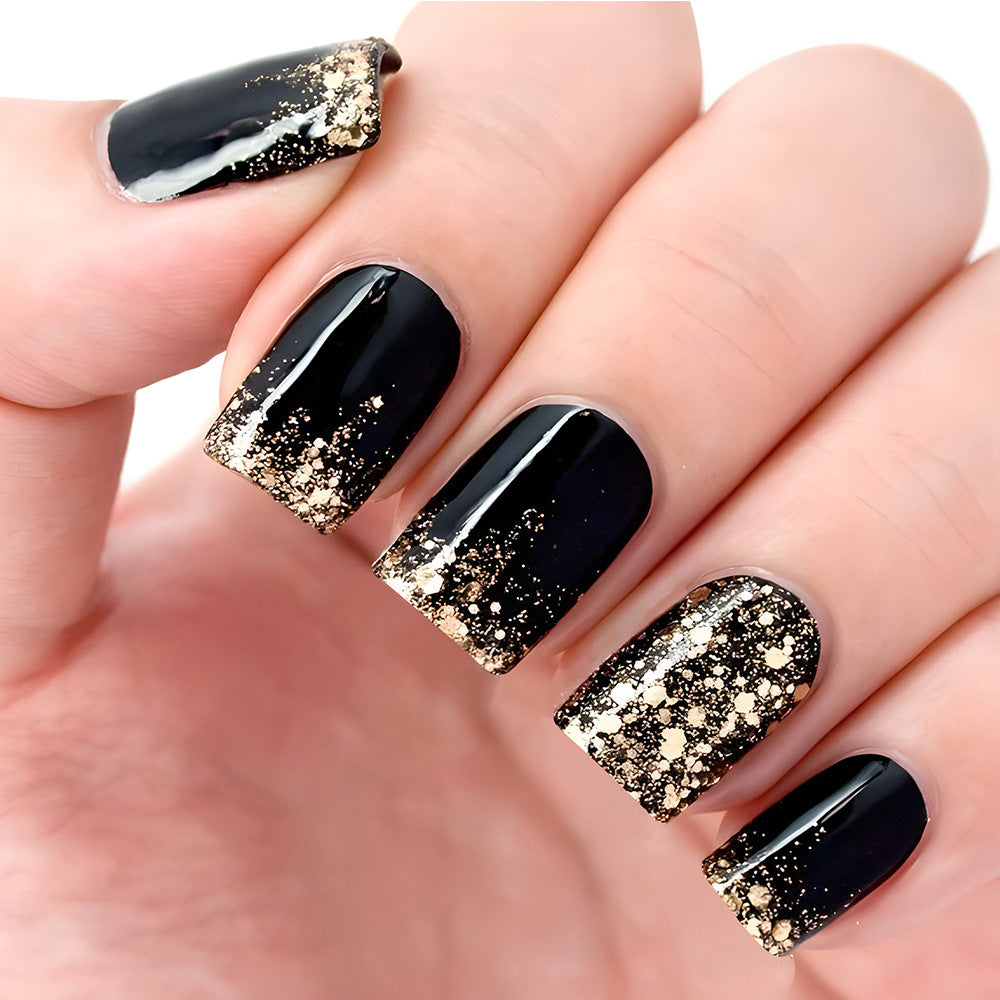 A hand showcasing press-on nails that are black with a gradient sparkle effect transitioning to gold.