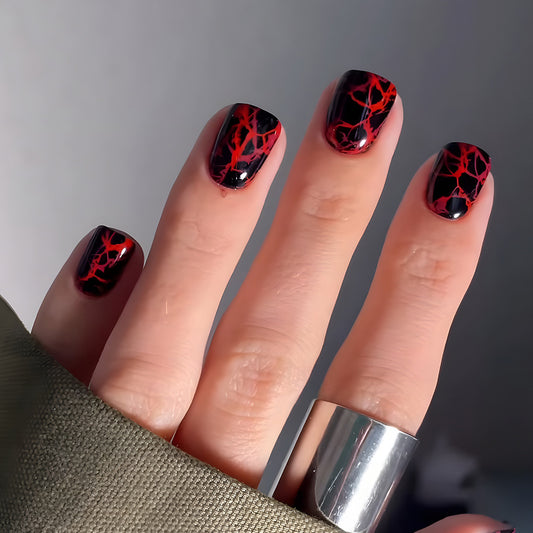 A set of press-on nails featuring a short square design with a black base and red vein patterns.