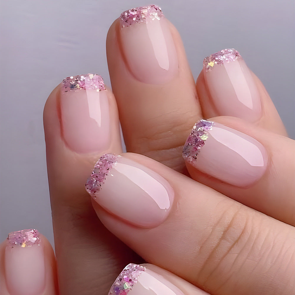 Close-up of a hand with pink nail polish and glittery accents on a neutral background