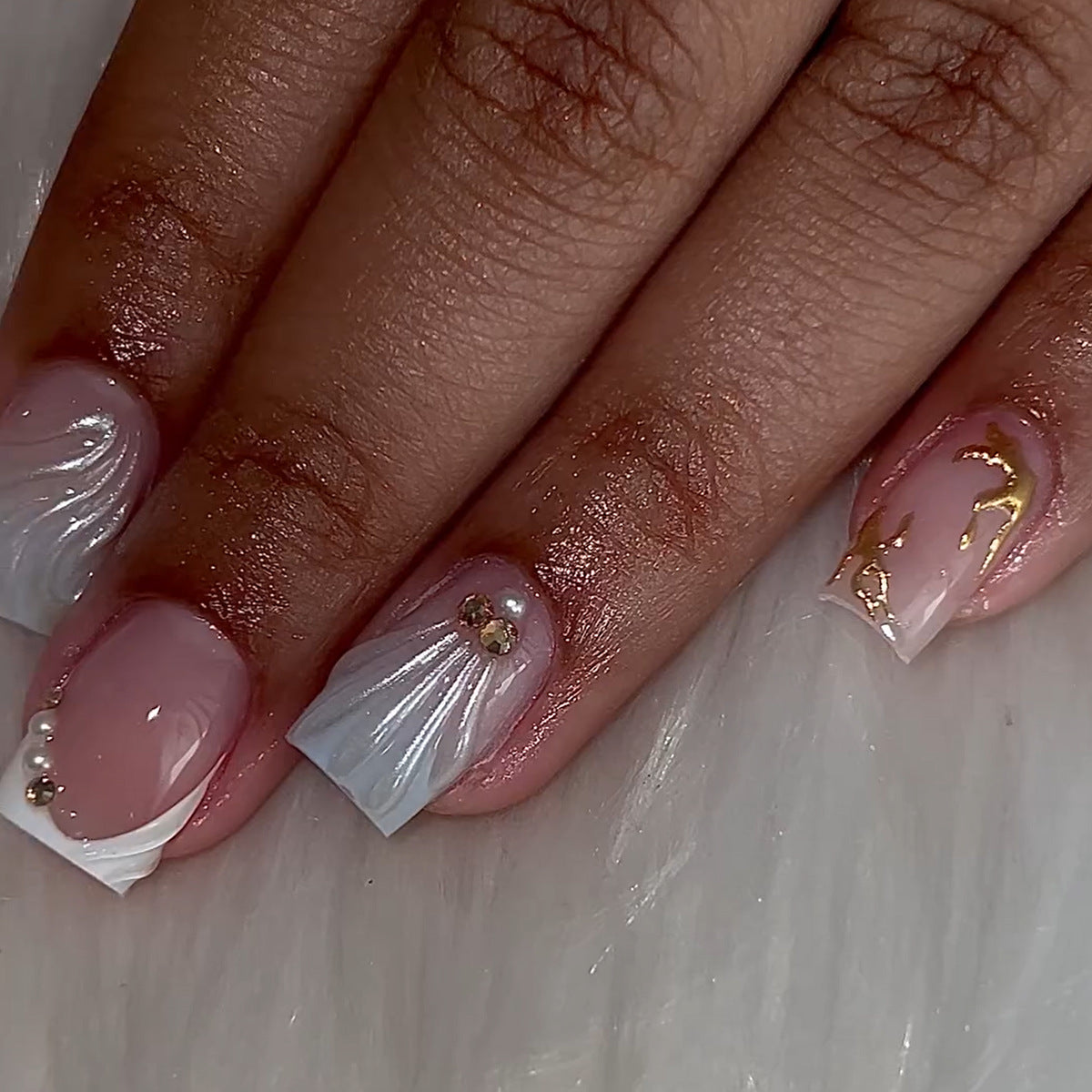 A set of press-on nails featuring a white and gold design with a textured finish.