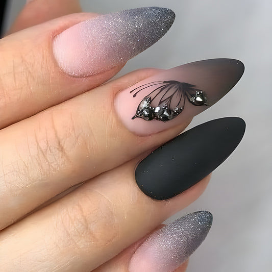 A set of almond-shaped press-on nails with a gradient of gray to black and intricate embellishments on the sidewalls.