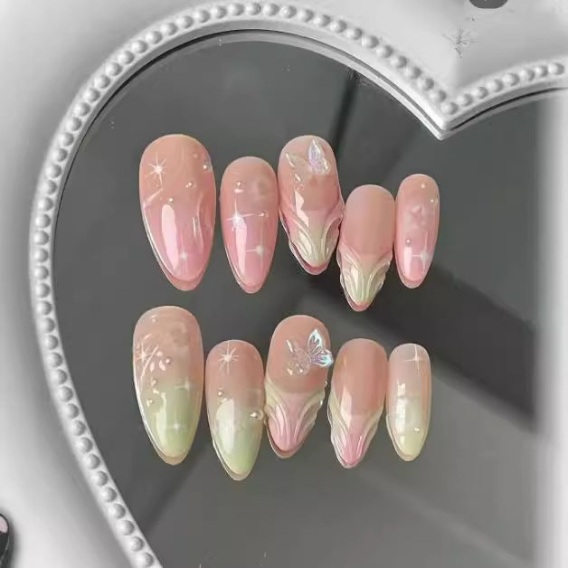 A set of long almond-shaped press-on nails with ombre gradient from pink to green and a sparkling butterfly accent on the top nail.