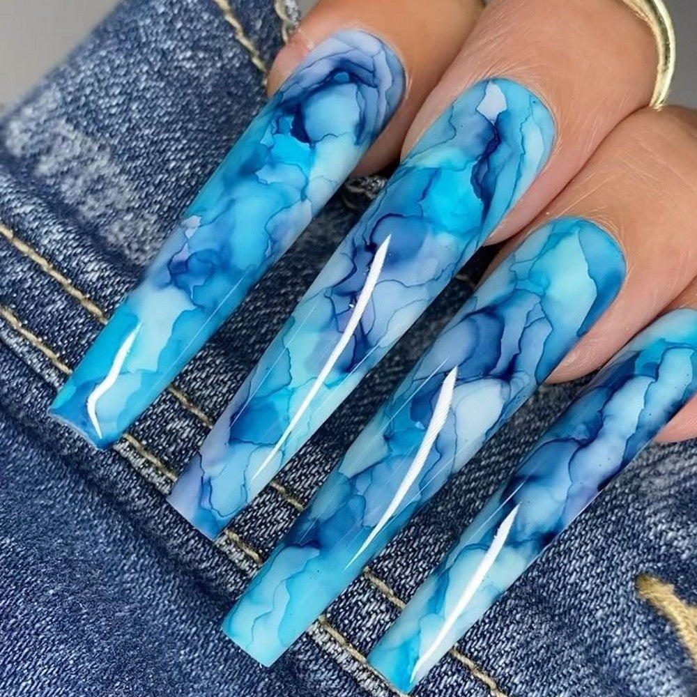 A set of extra-long coffin-shaped nails with a blue marble effect design, displayed on a denim background.