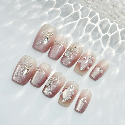 A set of blush pink press-on nails with long square shapes, adorned with pearls and gemstone accents.