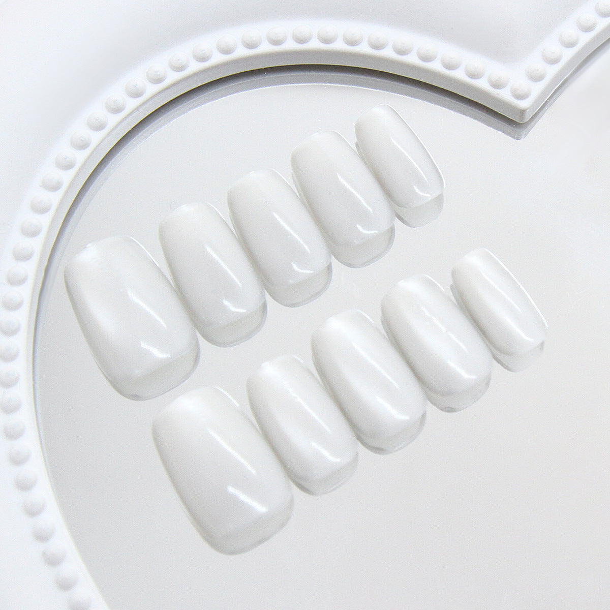 Set of white press-on nails on a white tray with decorative edge