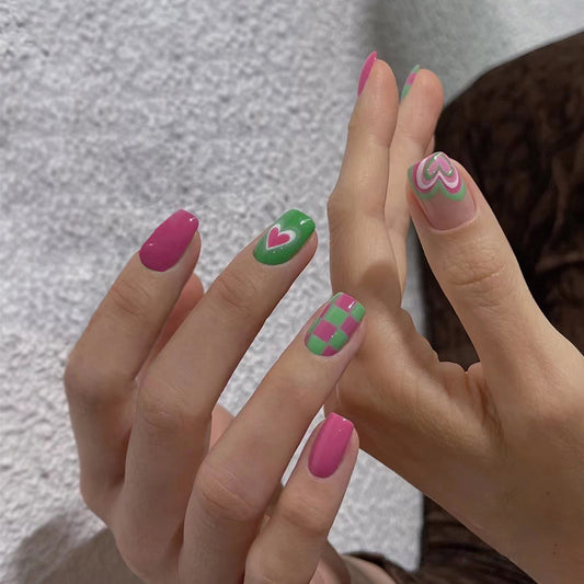 A set of press-on nails featuring a combination of pink and green colors with heart shapes and accents, displayed on a person's hands.