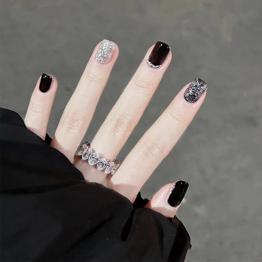 A set of press-on nails featuring a medium square black and silver glitter accent design on a person's hand.