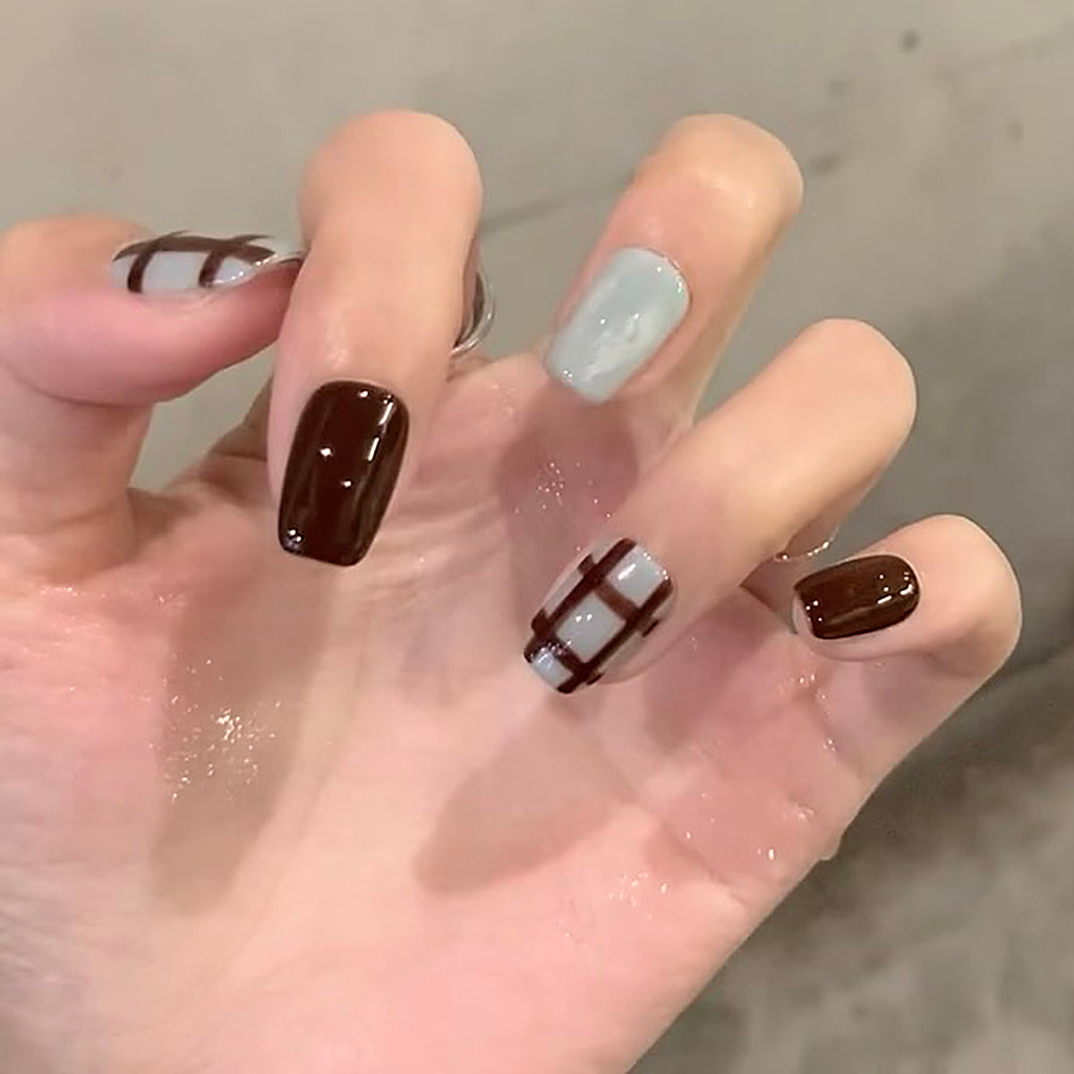A set of press-on nails featuring a medium length square design with brown and beige colors and a plaid accent.