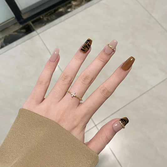 Hand with brown and black striped nail design on a neutral background
