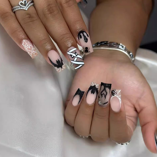 A set of long square press-on nails with black and beige design, featuring spider web and mummy motifs.