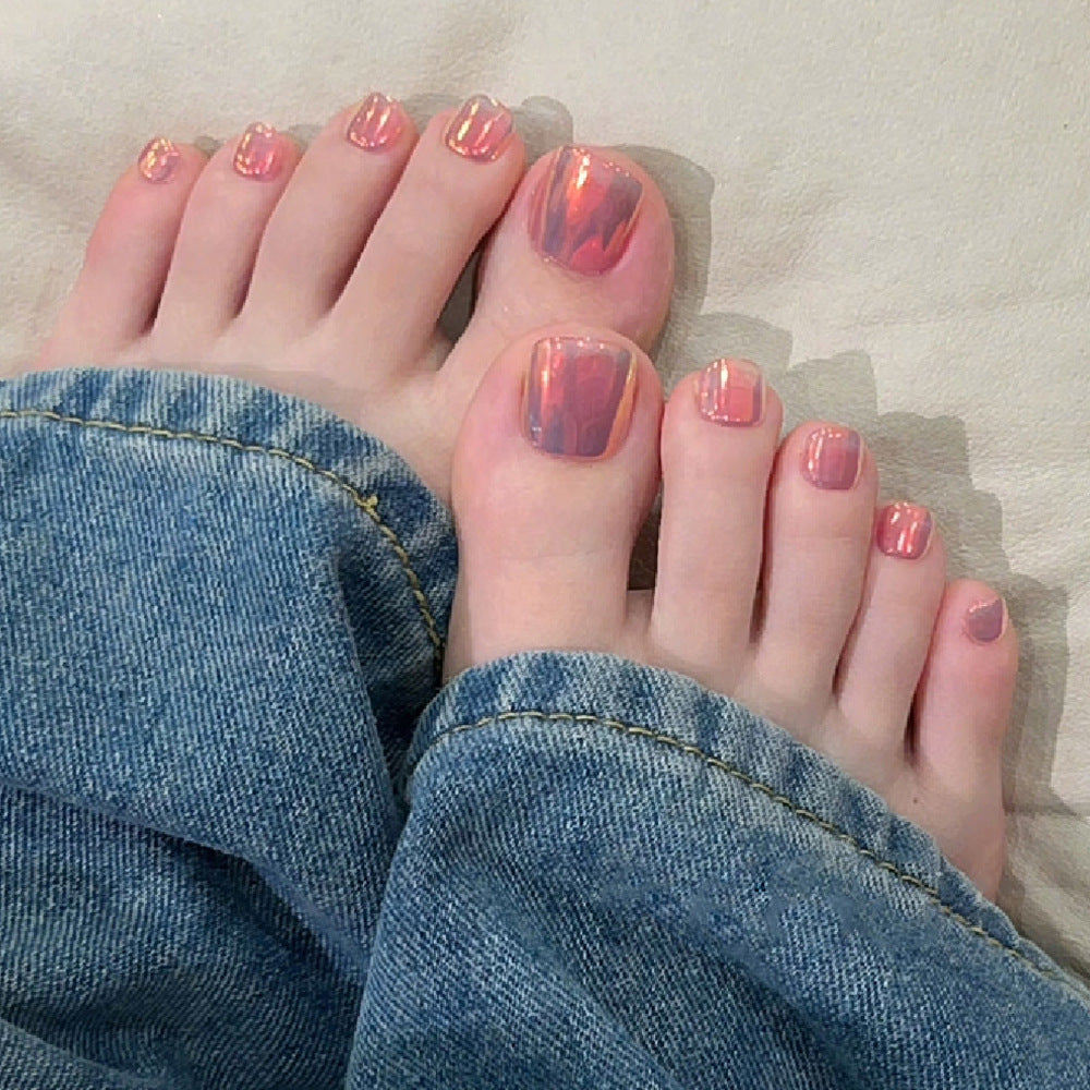 A pair of feet with short-length square peach press-on toenails with a reflective mirror finish.