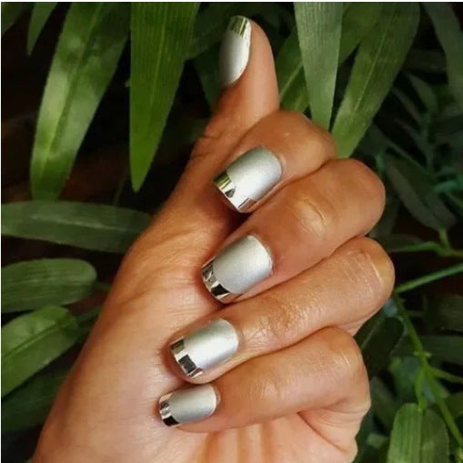 Hand with silver and white nail polish against a green leafy background
