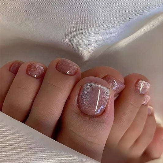 A close-up image of a person's feet with short square pink glitter finish press-on toenails.