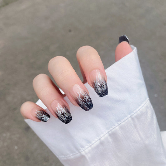A set of long, coffin-shaped nails with black glitter ombre design, displayed on a hand.