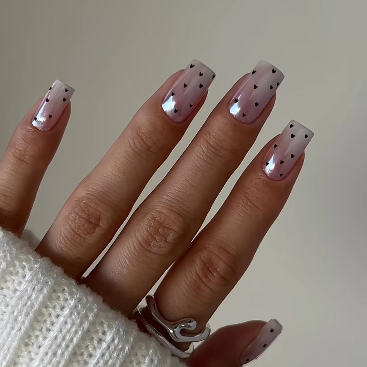 A pair of hands showcasing medium square beige and black heart pattern press-on nails.
