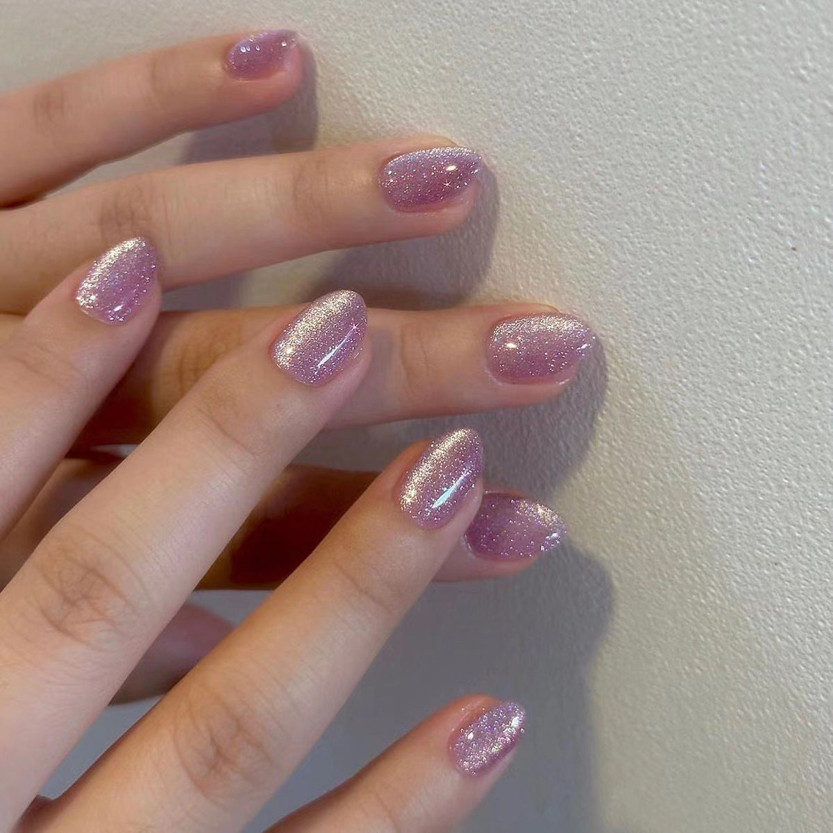 A close-up image of a person's hand with short oval-shaped press-on nails featuring a pink glitter finish.